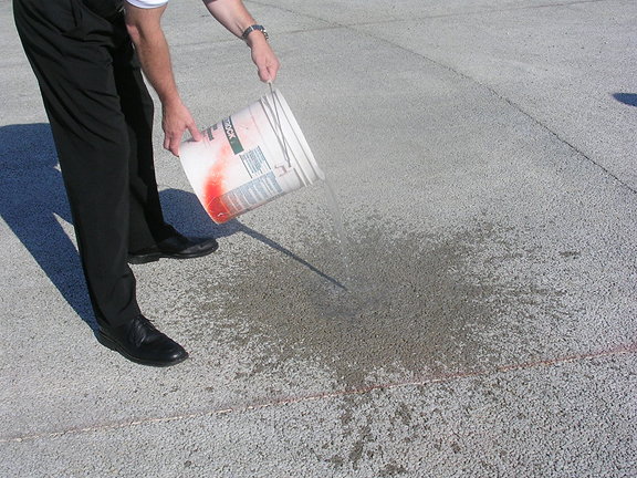Photo of person pouring water from a bucket onto the porous concrete. There is no pooling water, it immediately soaks into the porous concrete.