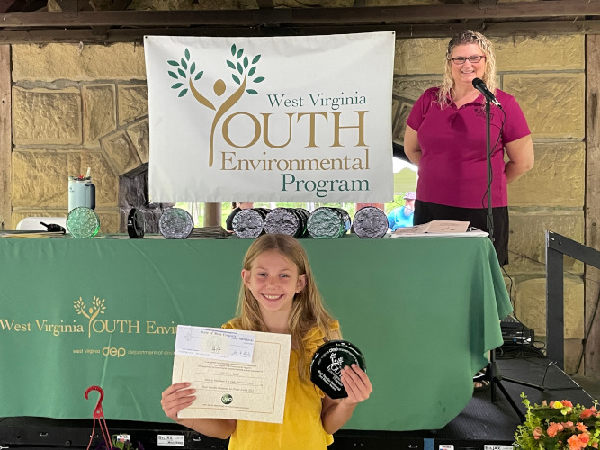 Ella Grant, from the Midway Meridians 4-H Club in Putnam County, smiles for the camera as she holds up her glass award, certificate and award check.